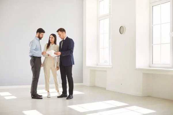 Three people reviewing paperwork together in a bright, empty property.