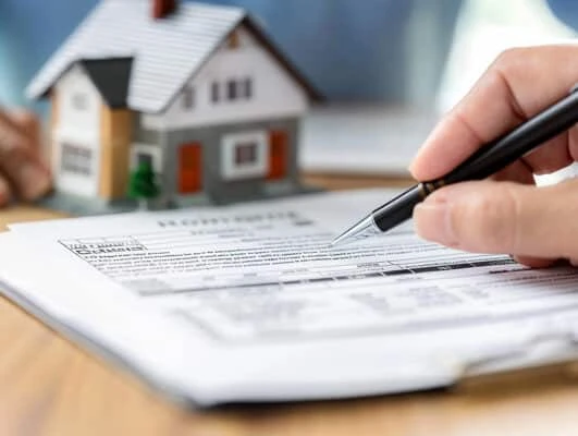 Landlord reviewing and signing a rental lease agreement with a property model on the table.