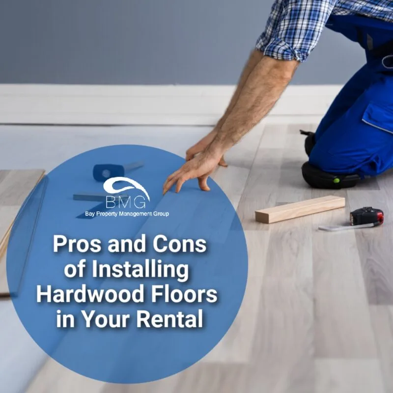 A person installing hardwood flooring, with a blue overlay containing text that reads, "Pros and Cons of Installing Hardwood Floors in Your Rental," under the Bay Property Management Group logo.