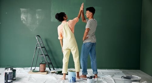 Man and woman high five while repainting a green wall.