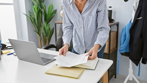 A person reviews documents at a desk with a laptop, preparing to amend HOA rules and regulations.
