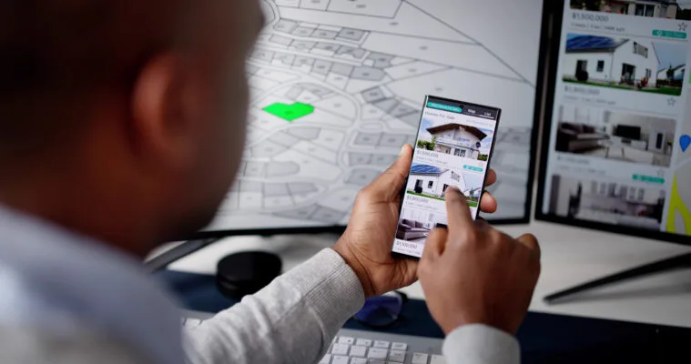 A person looking at apartment and house listings on their phone and computer.