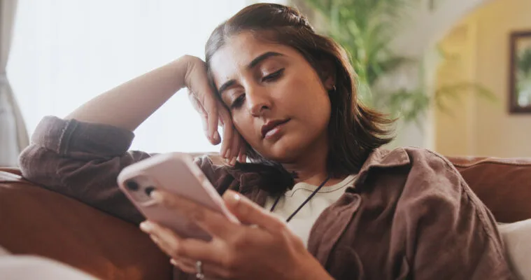 Woman on couch with smartphone, on social media looking at apartments.