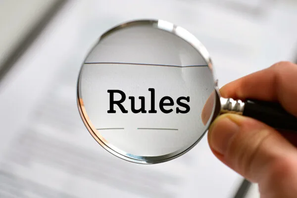 A hand holding a magnifying glass focusing on the word "rules" symbolizing scrutiny and attention to regulations