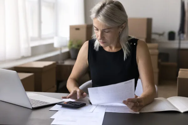 A woman using a calculator next to her laptop, as she holds a piece of paper