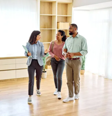 Agent holding a clipboard shows a couple around a bright apartment.