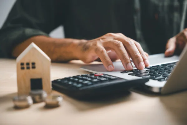 A man using his laptop, next to a calculator and toy model of a house