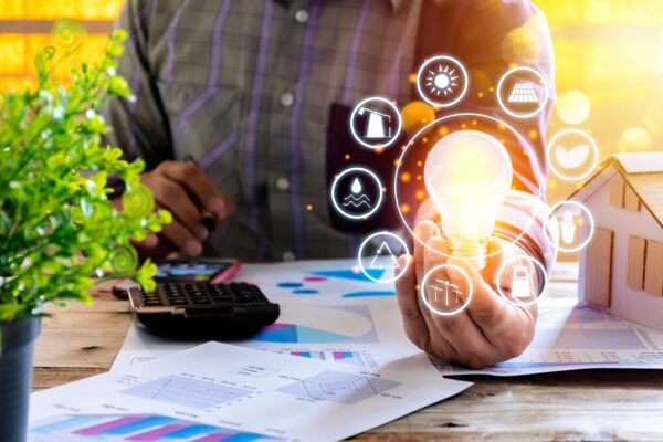 Businessmen calculate electricity bills using a calculator, graph, document. Lightbulb shining brightly next to him