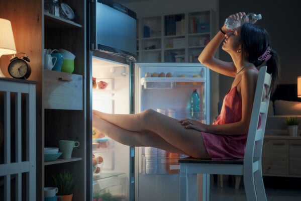 Woman suffering from the heat in summer, she is resting with her feet in the fridge and holding a water bottle