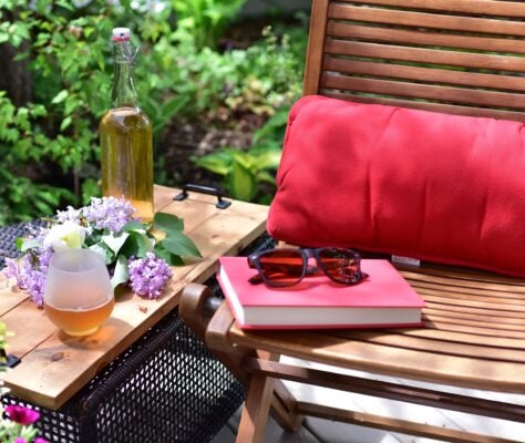 Outdoor patio seating with chair, a pink pillow, a book, and flowers