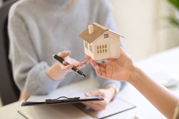 Person reviewing and signing rental property documents while holding a small model house.