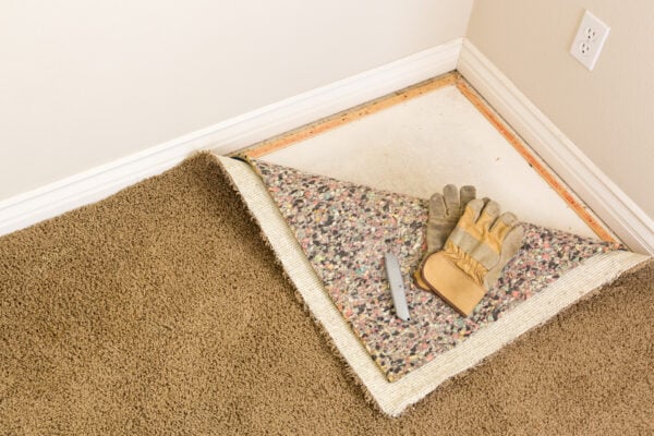 Partially removed carpet in a rental unit, showing padding and subfloor during replacement or inspection
