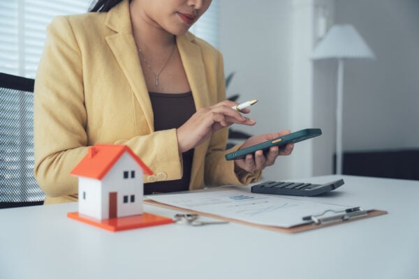 Real estate investor using a calculator with house model and financial documents, analyzing property profitability with the 1 percent rule.