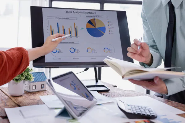 Two people reviewing charts and a sales analysis dashboard, representing how CMA reports use data to guide real estate decisions.