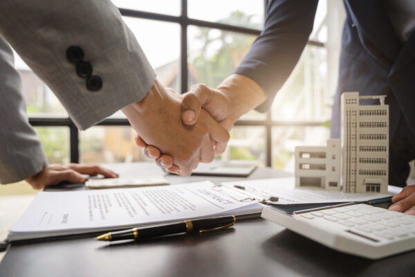Two professionals shaking hands over insurance documents, symbolizing commercial property coverage and landlord decision-making.
