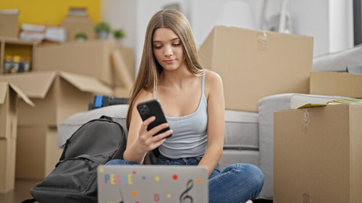 College student surrounded by boxes, managing rent and expenses online after moving into a new apartment.