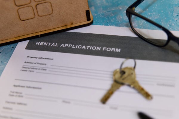 A close-up view of a rental application form with keys and reading glasses on a blue table, indicating a housing search.