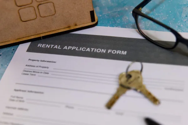 A close-up view of a rental application form with keys and reading glasses on a blue table, indicating a housing search.